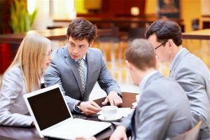 Divorce mediation: photo of three men and one woman sitting at conference table with laptop and coffee cup