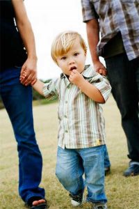 Mediation of Child Issues - photo of young boy dressed in jeans and striped shirt holding hands with mother and father is following behind