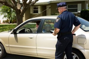 Teen drivers - photo of uniformed police officer walking up to white vehicle pulled over to side of the street