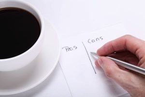 A hand holding a pen to make list of pros and cons while drinking coffee; the positive and negative effects of divorce