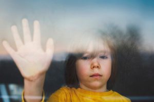 Sad child with hand against window; helping children of divorce avoid harmful narratives