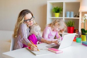 Woman balancing caring for two children while working on laptop computer and talking on cell phone, symbolizing default parent syndrome.